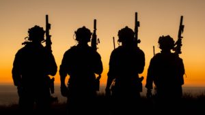 four soldiers standing with guns on a sunset background